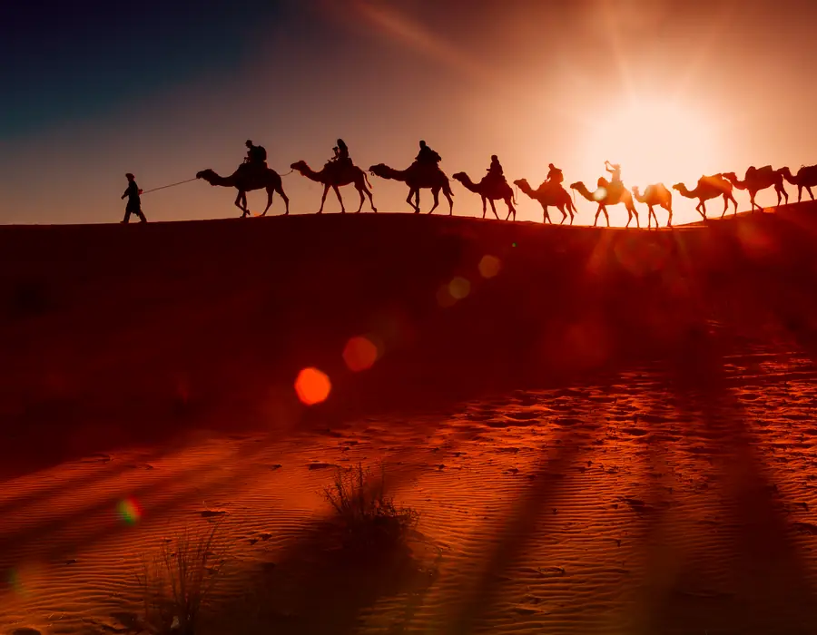 Caravana de camellos cruzando una duna al atardecer en el Erg Chebbi