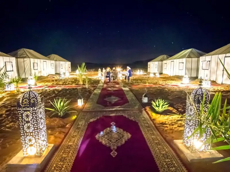 Campamento de lujo en el desierto de noche, con farolillos, alfombras y jaimas blancas