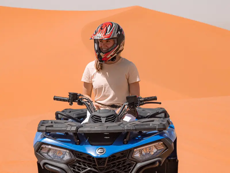 Rider on a blue quad bike in front of an orange dune