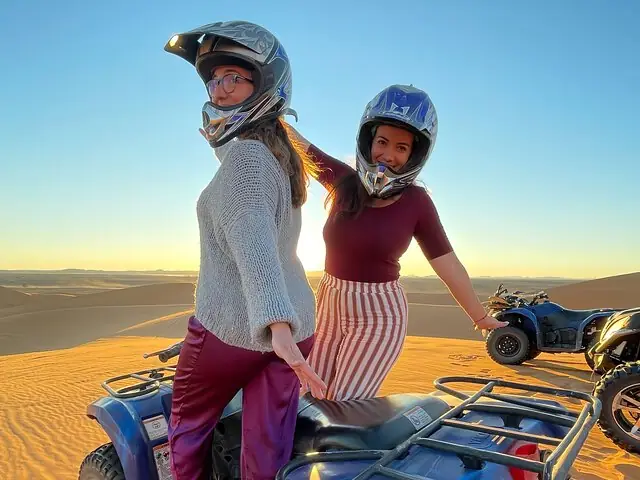 Dos viajeras con casco sobre un quad al atardecer en las dunas de Merzouga
